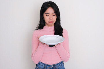 Young Asian woman looking to empty dinner plate that she hold with sad expression