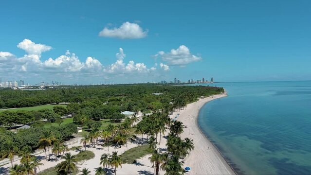 sideways aerial footage of skyscrapers, hotels and office buildings and ocean water in the city skyline and the lush green palm trees and grass at Crandon Park in Key Biscayne Florida USA