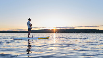 A man on a paddle board in the rays of sun. - obrazy, fototapety, plakaty