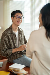 A happy Asian man in glasses is talking and sharing his ideas with a female friend in the room.