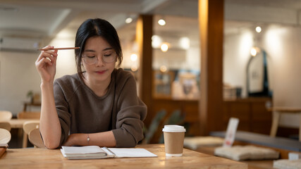 A focused female college student working remotely at a coffee shop, reading a book or doing homework