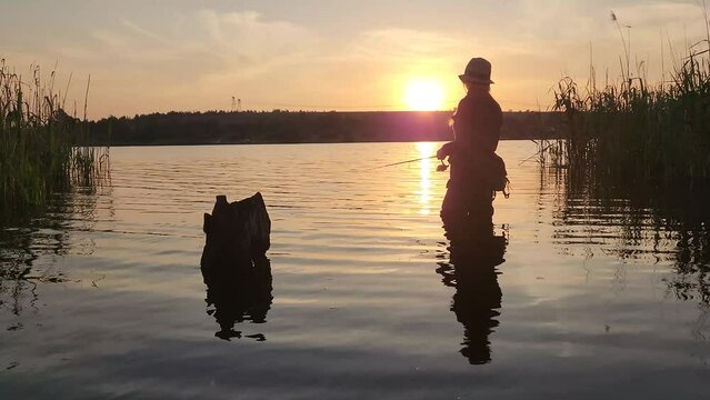 A girl fishing in a calm lake with a perfect sunset in the distance
