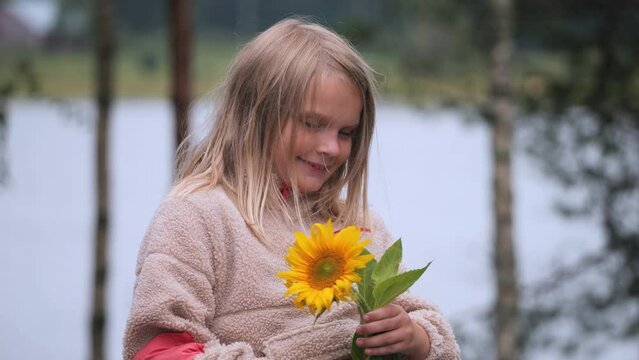 Cute little girl holds sunflower in hand and smiles, portrait view