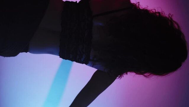 Vertical video. Oriental performance. Modern dance. Graceful sensual woman in black lace lingerie moving on blue pink neon light background.