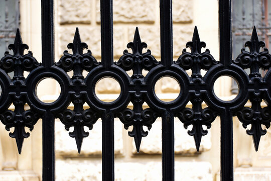 decorative vintage style black cast iron fence closeup detail, frontal, flat on view. Burggarten, Vienna, Austria. blurred beige stucco exterior elevation beyond. arts and architecture. steel pickets