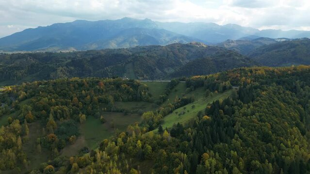 Aerial view of an autumn scene in a Transylvanian village with a view of high mountains. Bucegi mountains in Romania. A mountain village and green trees. Peștera, Romania