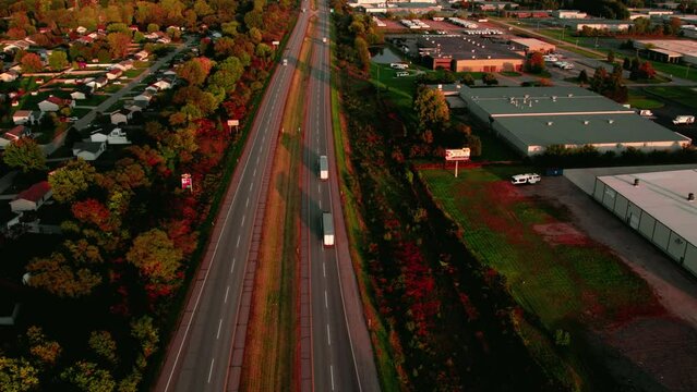 Semi Truck and trailers driving on Indiana Toll Road I-80. Interstate full with truck drivers, reefers, dryvans, flatbeds, conestoga and stepdecks. High angle aerial sunset in Elkhart Indiana.