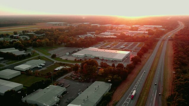 Red semi truck and trailer driving at magic hour on Indiana Toll Road  I-80 Elkhart Indiana. Dryvan, reefer, car hauler carriage, flatbeds on highway.Warehouse shippers on left, forest on right.