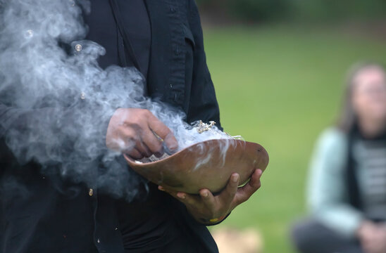 Human hands hold wooden ceremonial dish with smoked branches, the welcome ritual rite at an indigenous community event in Australia