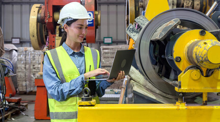 A dedicated female engineer dressed in safety gear, holding laptop computer amidst a sprawling factory.