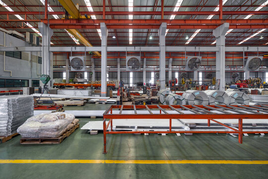 Metal sheets and steel sheet roll are placed on the floor in metal sheet factory. Large crane and truck are in the working area.