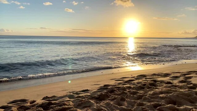 Bright golden sun casts ray of light across open ocean as gentle waves crash on sandy shores of Hawaii