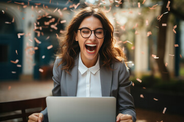 Happy young businesswoman celebrating achievement or online success while looking at laptop screen.