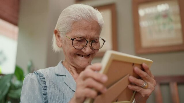 Happy Asian elderly older grandmother holding family photographs on hands and hugging while missing moments and memory of life. Elderly older lifestyle concept