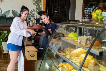 Asian beautiful woman employee wear apron stands at counter taking orders from customers, happy barista recommending new menu, Small business coffee shop owner talk to clients restaurant guests.