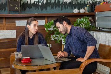 Two businessman and woman discuss working together with laptop computer at coffee shop, Colleagues share experiences and laugh while drink coffee, Small business owner couple working together.