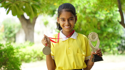 Excited Indian student school child wearing school uniform holding victory trophy in hand,...