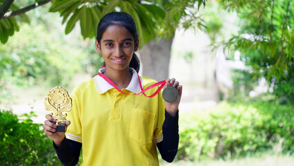 Excited Indian student school child wearing school uniform holding victory trophy in hand,...