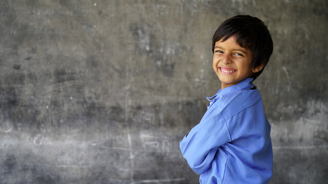 Cute Happy Indian school boy wearing uniform in the classroom near the chalk board
