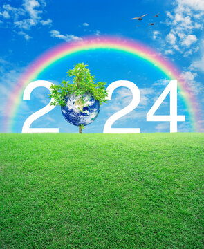 2024 white text with planet and tree on green grass field over rainbow, birds and blue sky, Happy new year 2024 ecological cover, Save the earth concept, Elements of this image furnished by NASA