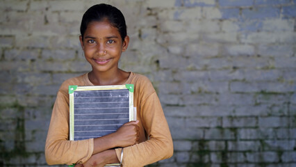 Rural School girl holding slate with English alphabet. Indian child writing A B C D alphabet on...