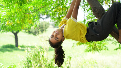 Happy smiling girl hanging on a tree. The child laughs happily. Spring mood. Active lifestyle. Tree climbing.