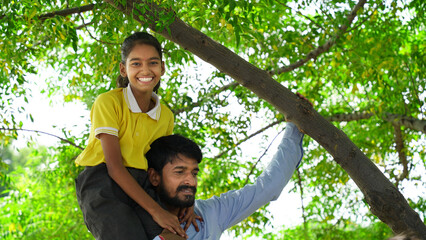 Portrait of lovely daughter smiling and sitting on the neck of her handsome father isolated over nature background