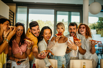 Friends having a blast at a daytime house party, taking photos, munching on pizza, and enjoying drinks. - obrazy, fototapety, plakaty