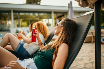 A diverse group of friends having a great time at a yard party. They're lounging by the pool, chatting and drinking.