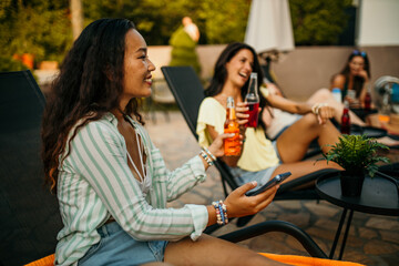 An Asian woman with a bunch of friends having a blast at a poolside gathering. They're laughing, sipping on drinks, and snapping selfies in the yard