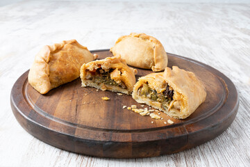 In the foreground, a Cocarrois cut into pieces with other empanadas next to it. All on a round brown wooden board on a white background. Typical Mallorcan food