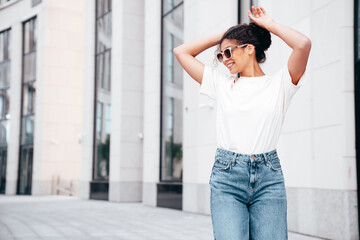 Fototapeta na wymiar Young beautiful smiling hipster woman in trendy summer white t-shirt and jeans clothes. Carefree woman, posing in the street at sunny day. Positive model outdoors. Cheerful and happy. in sunglasses