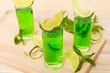 Sweet refreshing mint liqueur, with ice and mint leaves on table background, Shots with lime slice and mint flat lay