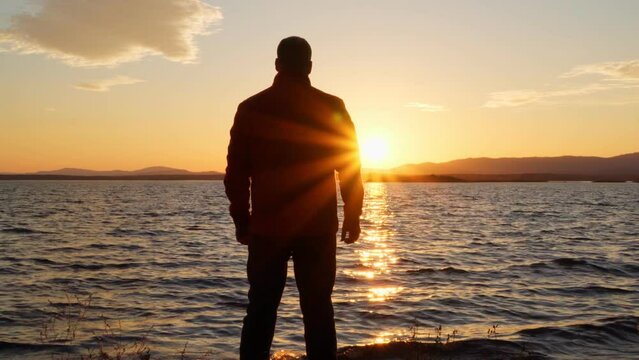 A lonely man stands on the shore of a lake at sunset and admires the beauty of nature. Harmony of nature and man.
