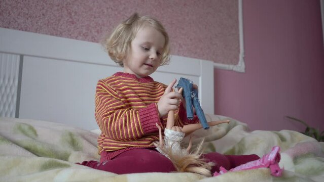 a little girl dresses a doll,the girl plays with a doll, puts jeans on the doll's legs