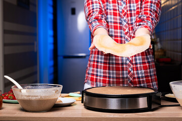 Woman cooking delicious crepe on electric pancake maker in kitchen, closeup