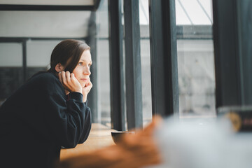 Sad woman sitting by the window looking outside