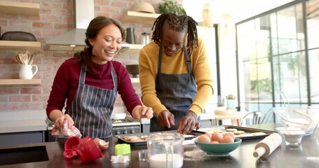 Happy diverse couple in aprons baking christmas cookies in kitchen, slow motion - Powered by Adobe