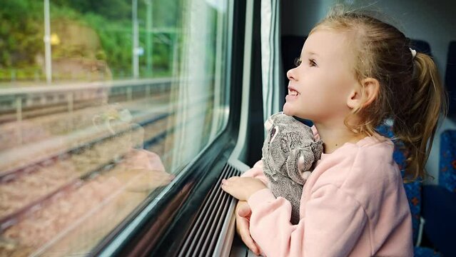 Little girl looking out train window outside, during moving. Traveling by railway in Europe