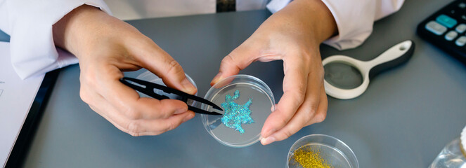 Banner of unrecognizable female chemist examining blue glitter in facial cream sample over petri dish on environment research laboratory. Scientist studying microplastics on cosmetic composition. - obrazy, fototapety, plakaty