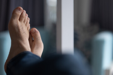 Closeup of a man's feet, relaxing on a bed in a hotel room. In the background is an upholstered...