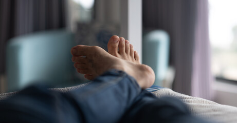 Closeup of a man's crossed leg, showing his feet relaxing and hanging off the edge of a bed in a...