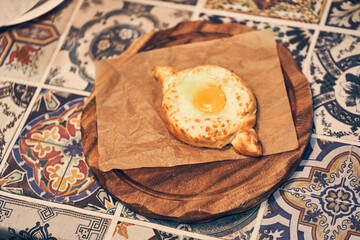 Traditional Georgian pastries - khachapuri in Adjarian style with cheese and raw yolk. Khachapuri with egg on a wooden stand. Khachapuri in Adjarian style with ingredients. High quality photo