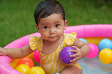 Fototapeta na wymiar infant baby girl playing water with colorful plastic balls in inflatable pool