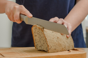 Kobieta kroi nożem do chleba chleb, z bliska - obrazy, fototapety, plakaty