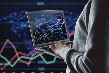Close up of hacker hands using laptop with glowing downward red forex chart on blurry dark background with index grid. Crisis, hacking and stock market fall concept.