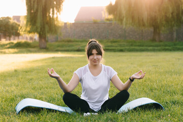 Fototapeta premium The girl sits on a log and relaxes against the background of the sunset and nature. Yoga at sunset.