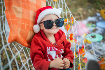 baby in santa claus hat and sunglasses lying on a hammock