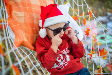 baby in santa claus hat and sunglasses lying on a hammock