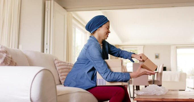 Happy biracial woman in hijab unpacking boxes at home, copy space, slow motion